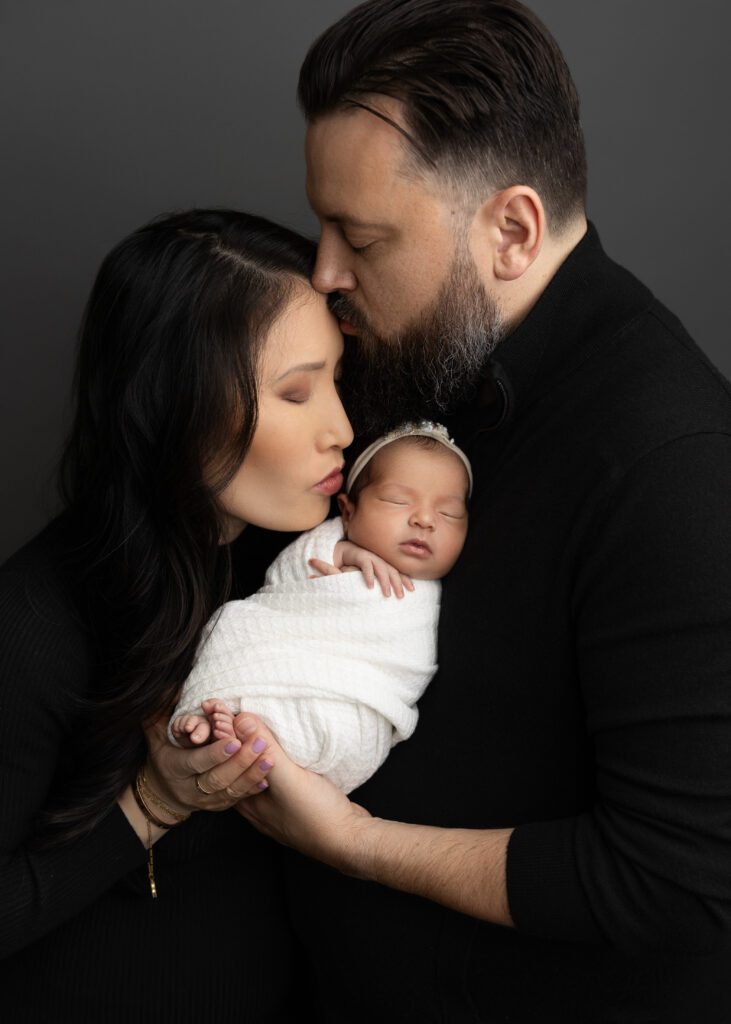Dad kissing mom, mom kissing baby emersyn